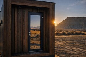 A wooden structure with a door, a view of a desert landscape, and a mountain range in the background.