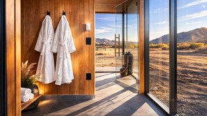 A modern bathroom with wooden walls, two white towels, and a view of a desert landscape through large glass doors.