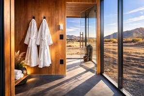 A modern bathroom with wooden walls, two white towels, and a view of a desert landscape through large glass doors.