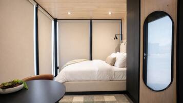 Ein gemütliches Schlafzimmer mit einem Bett, einem kleinen Tisch mit einer Pflanzenbowl und einem großen Fenster.