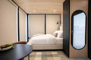 Ein gemütliches Schlafzimmer mit einem Bett, einem kleinen Tisch mit einer Pflanzenbowl und einem großen Fenster.