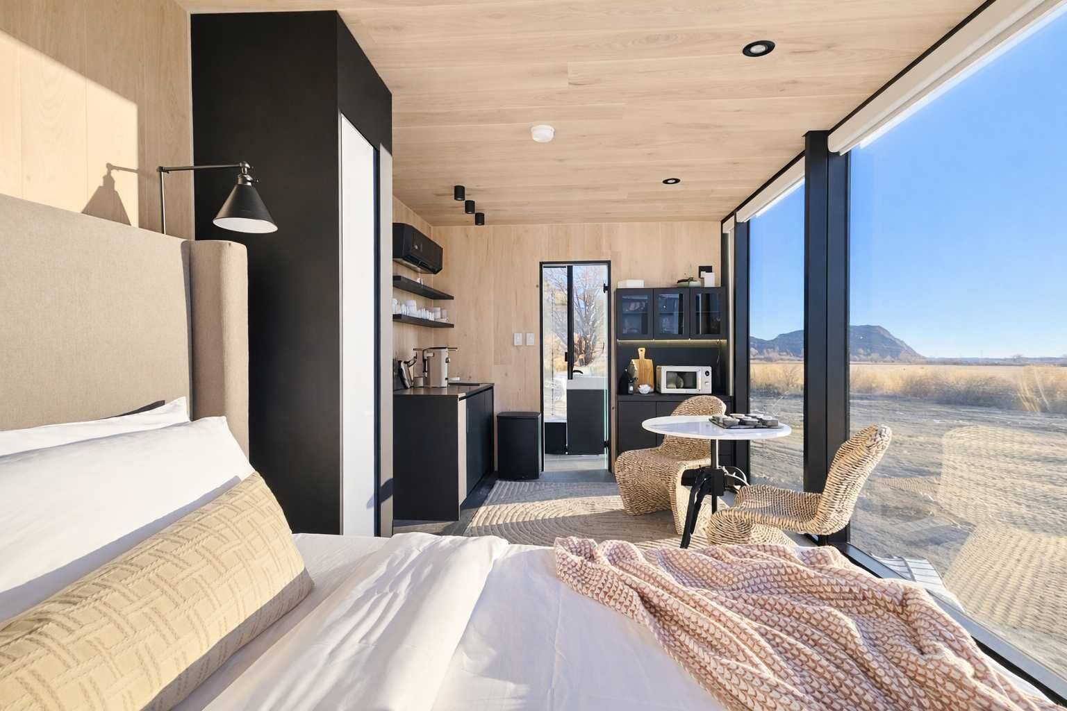 A modern bedroom with a large bed, a small table, and a view of a desert landscape.