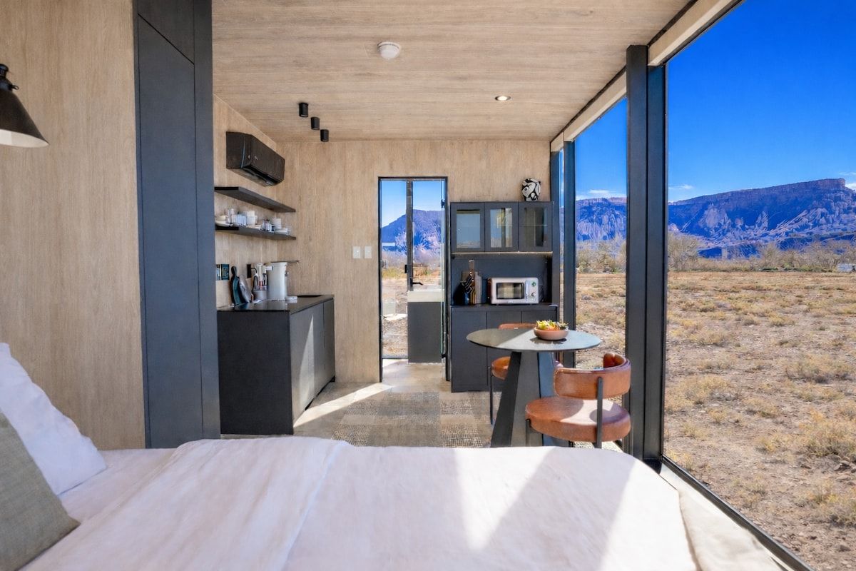 A modern bedroom with a large bed, a small dining area, and a view of a mountainous landscape.