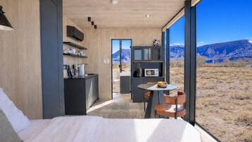 A modern bedroom with a large bed, a small dining area, and a view of a mountainous landscape.