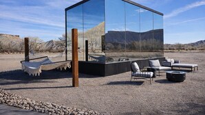 A modern glass structure with outdoor seating and a hammock.