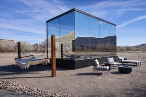 A modern glass structure with outdoor seating and a hammock.