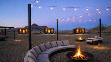 An outdoor seating area with a curved sofa, a fire pit, and string lights.