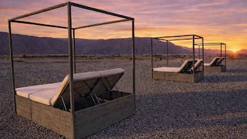 Outdoor lounge chairs with a metal frame and woven seat, set on a gravel surface with a mountainous backdrop.