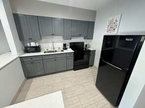 A modern kitchen with grey cabinets, a black refrigerator, and a white countertop. - Englewood Inn & Suites (Englewood)