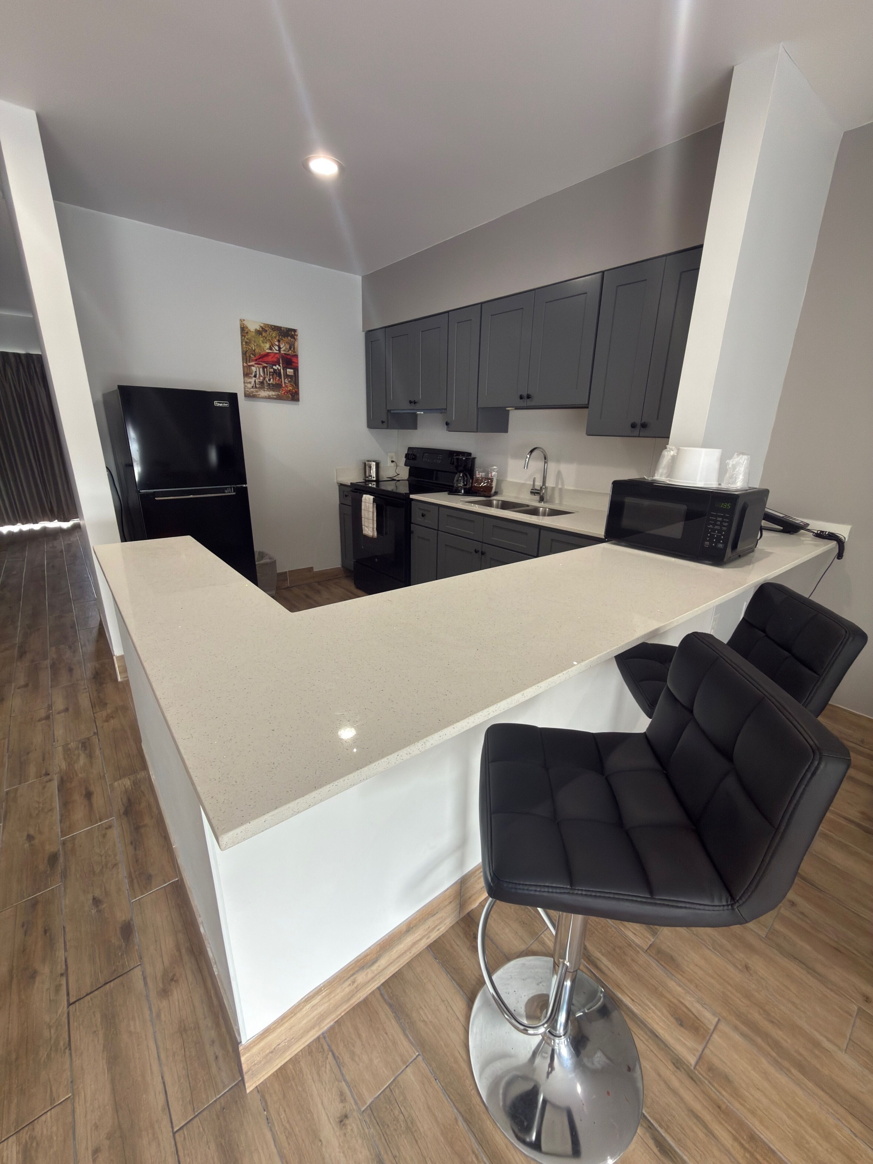 A modern kitchen with a central island, bar stools, and a black refrigerator.