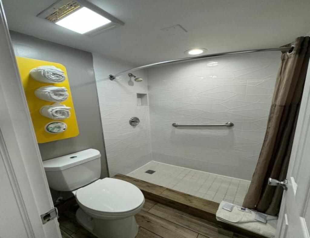 A small bathroom with a toilet, a shower with a glass door, and a yellow towel rack.