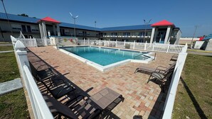 Ein Poolbereich mit Pflasterterrasse, Liegestühlen und einem weißen Zaun.