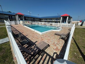A pool area with a brick patio, lounge chairs, and a white fence. - Englewood Inn & Suites (Englewood)