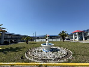A courtyard with a central fountain, surrounded by a white fence, and a building with a red roof in the background. - Englewood Inn & Suites (Englewood)