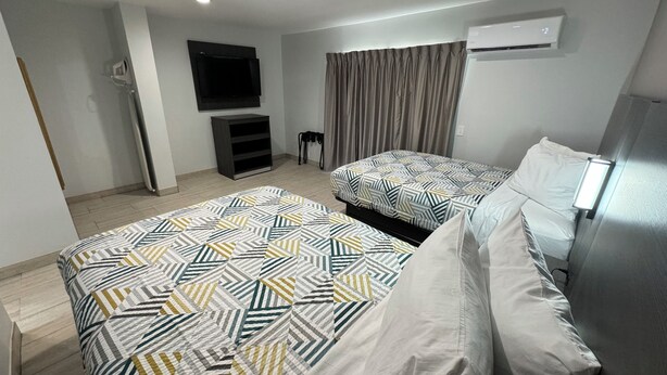 Ein modernes Hotelzimmer mit zwei Betten, einem Flachbildfernseher, einer Klimaanlage und einem Fenster mit Vorhängen.