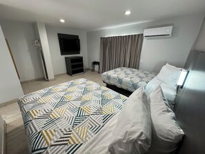 Una habitació d'hotel moderna amb dos llits, un televisor de pantalla plana, un aire condicionat i una finestra amb cortines.