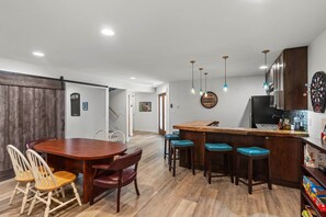 A modern kitchen with a wooden dining table, bar stools, and a dartboard. - Chamber's Bay Lodging (University Place)