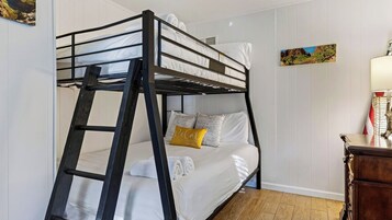 Una cama litera con escalera, ropa de cama blanca, una almohada amarilla y una mesita con lámpara.