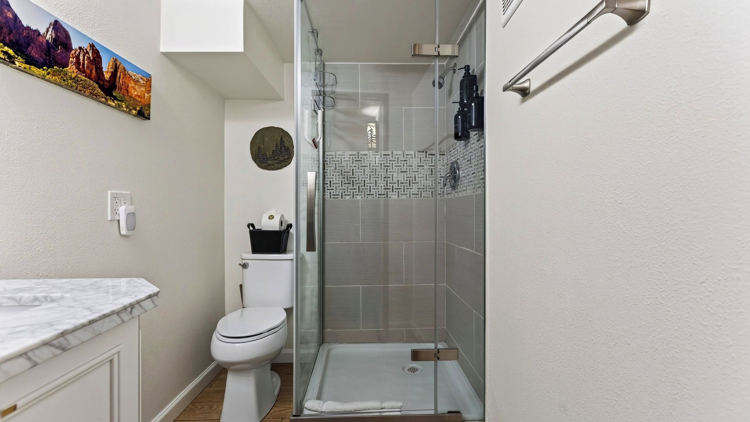 A bathroom with a toilet, a shower enclosure, and a marble countertop.