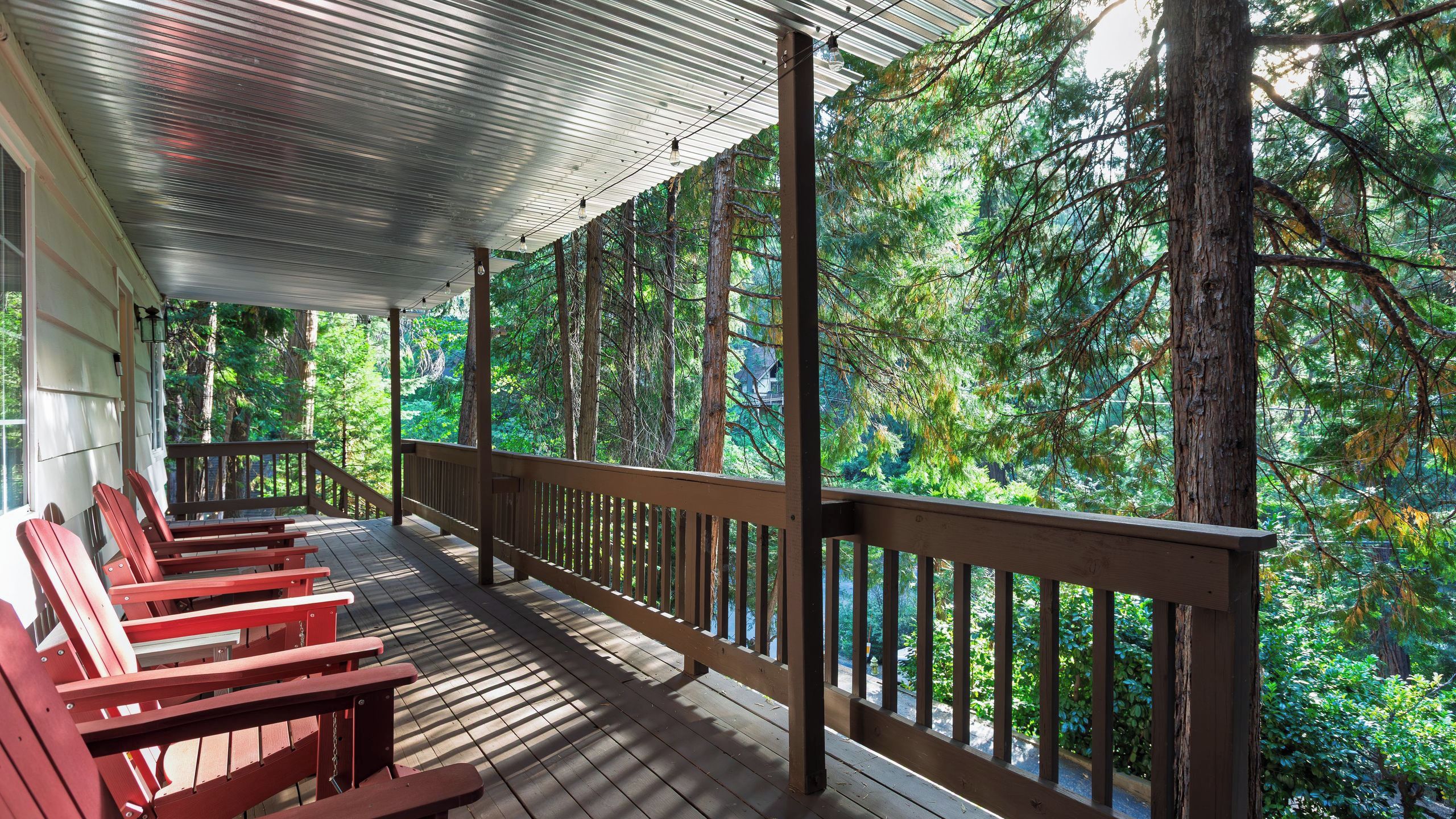 A covered porch with wooden railings and benches, overlooking a forested area.