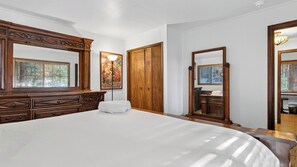 A bedroom with a large bed, wooden dresser, wardrobe, and a mirror. - Wilderness Lodge by Avantstay Firepit Gazebo + Wraparound Decks Minutes to Village + Trails (Cedar Glen)