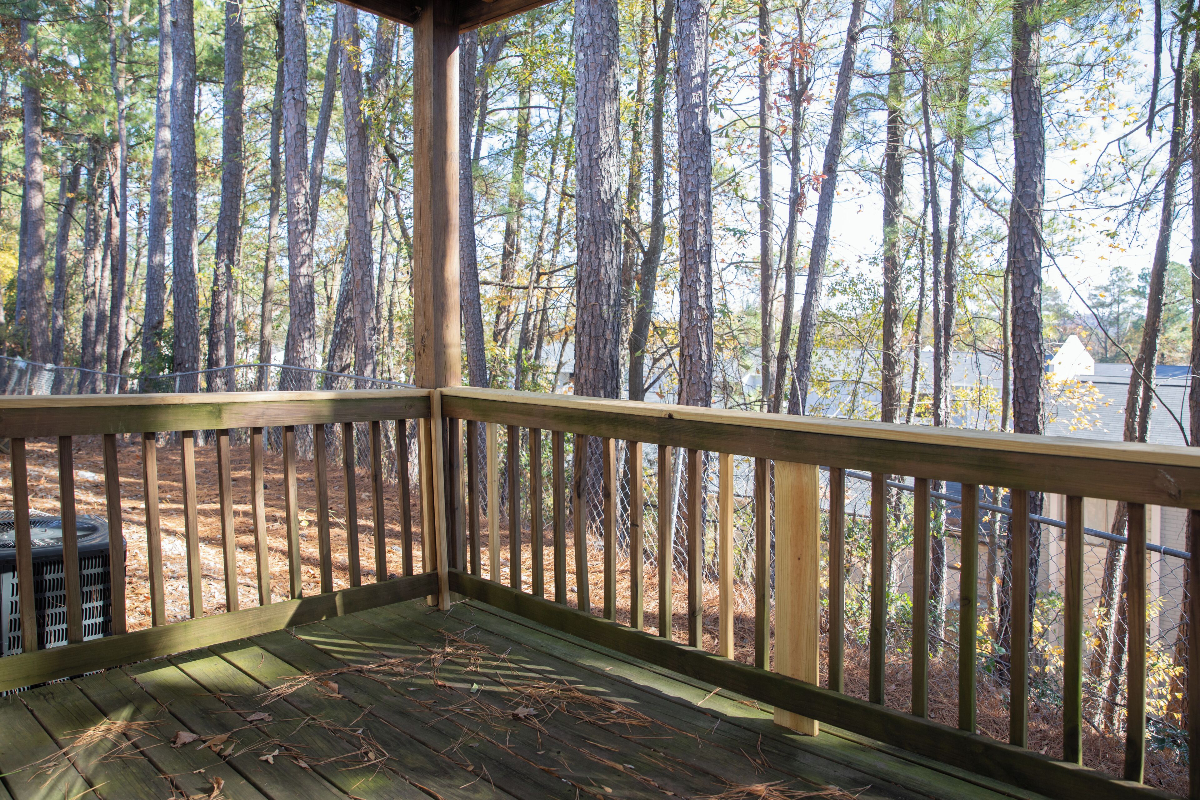 Une terrasse en bois avec une rambarde en métal, donnant sur une zone boisée.