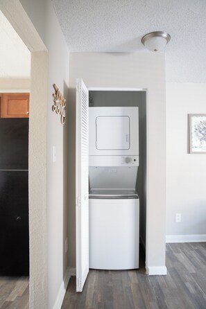 Une petite buanderie équipée d’un lave-linge et d’un sèche-linge intégrés, d’un meuble en bois et d’une enseigne décorative.