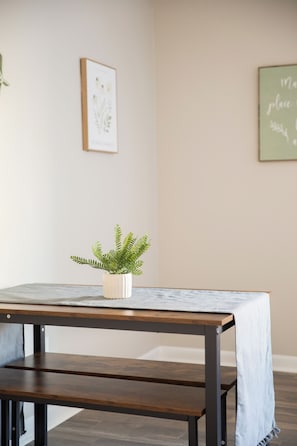 Una habitación con una mesa de madera, una planta en maceta y dos cuadros en la pared.
