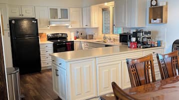 Una cocina moderna con armarios blancos, un refrigerador negro, una mesa de comedor de madera y una cafetera.