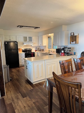 A modern kitchen with white cabinetry, a black refrigerator, a wooden dining table, and a coffee machine.