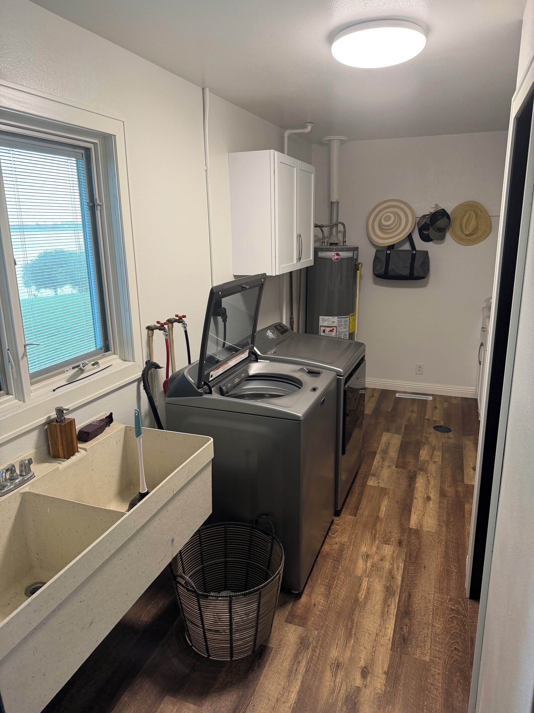 Cocina compacta con lavadora y secadora integradas, una ventana con persianas y un pequeño cubo de basura.