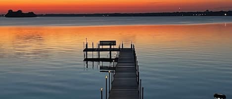 A wooden pier extending into calm water, with a bench and lamp posts along its length.