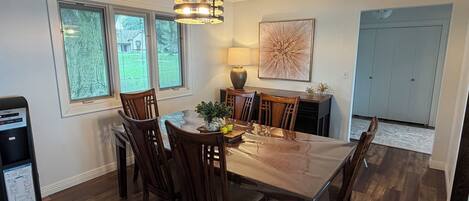 A dining area with a wooden table and chairs, a chandelier, and a large window.