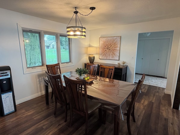A dining area with a wooden table and chairs, a chandelier, and a large window.