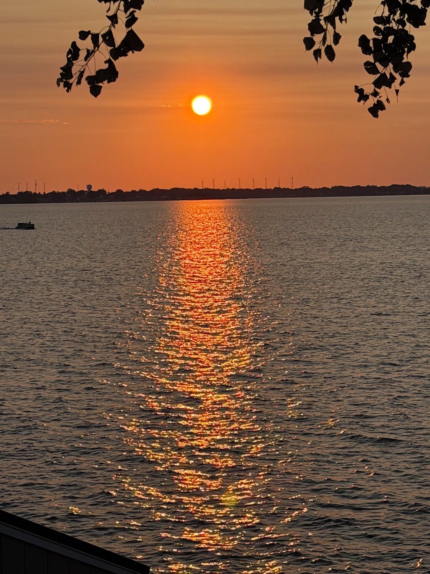 Un coucher de soleil sur une étendue d’eau, avec un bateau et des éoliennes visibles au loin.