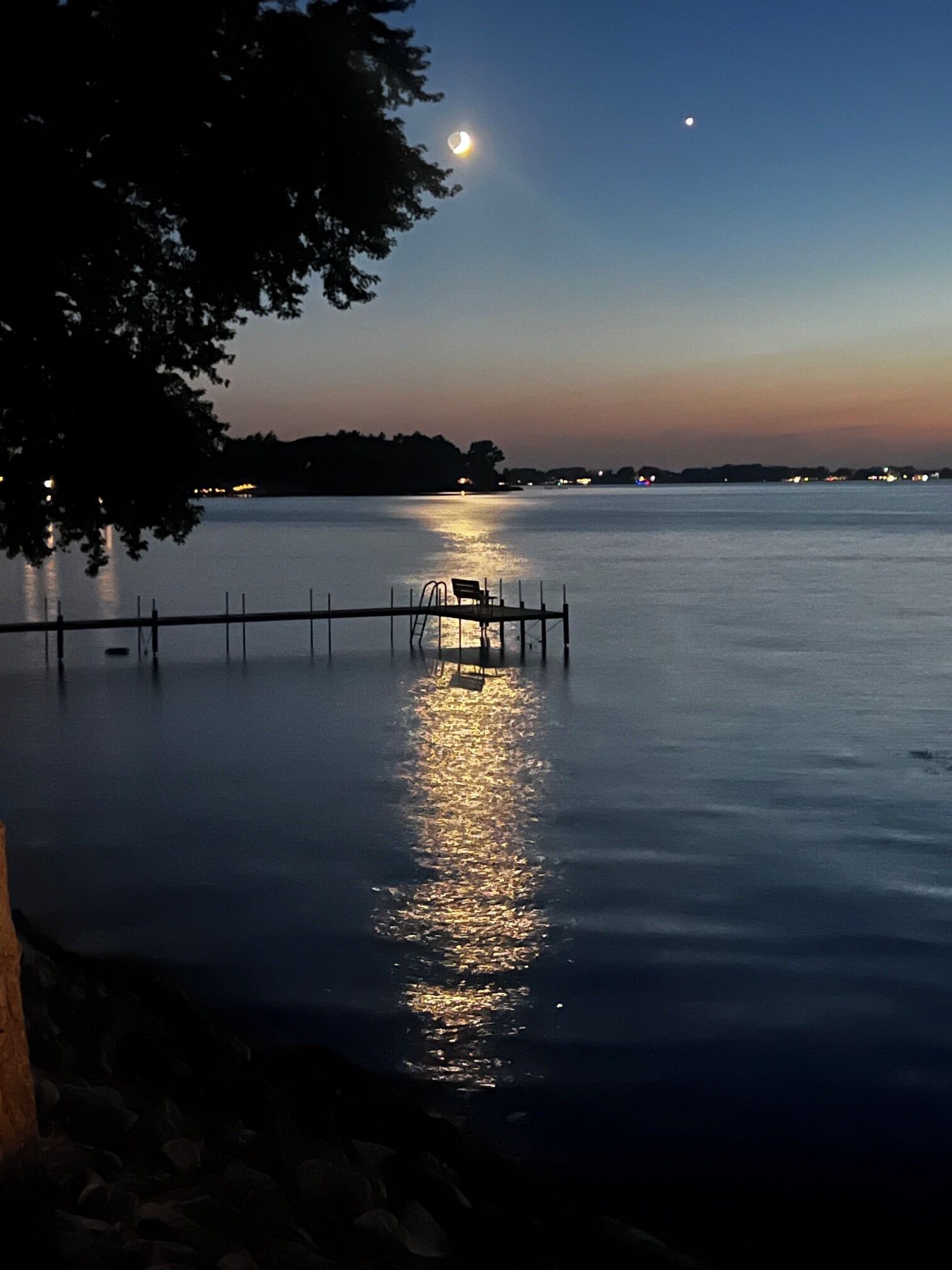 Un plan d’eau calme avec une jetée qui s’avance sur l’eau, un banc sur la jetée et un arbre sur la gauche.
