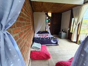 Un dormitorio con una cama, una mesita pequeña y un ventanal.