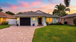 A residential house with a brick driveway, a garage, and a well-maintained lawn.