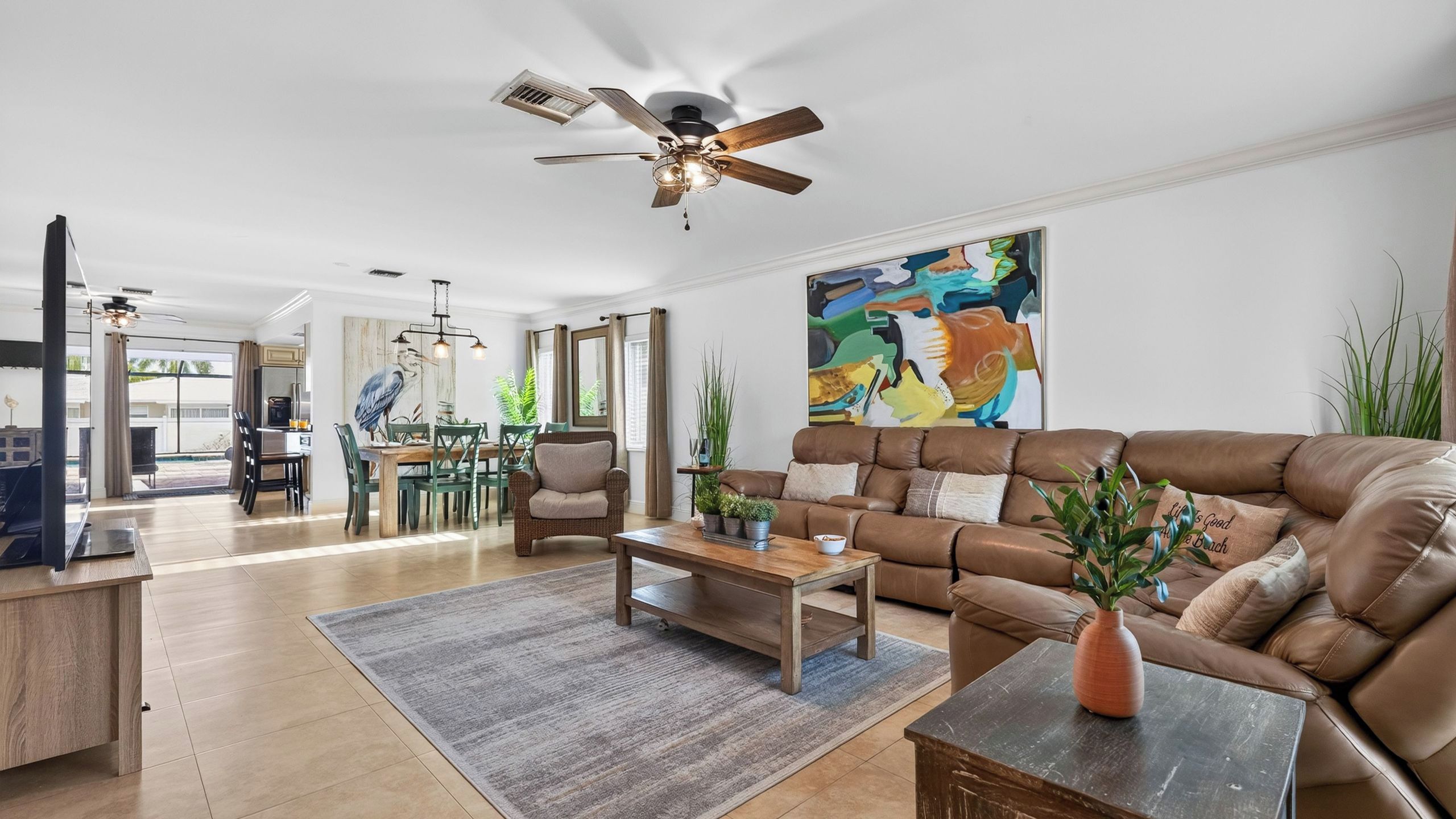 A spacious living room with a brown leather sofa, a wooden coffee table, and a dining area with green chairs.