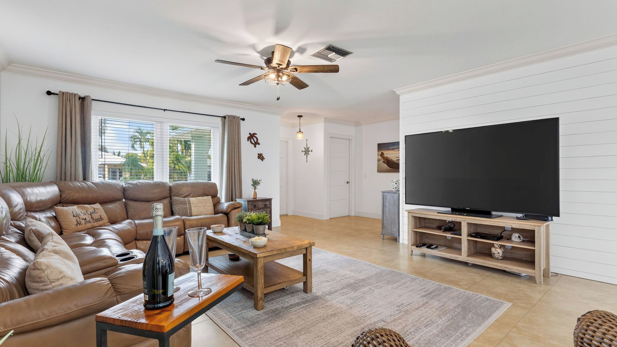 Een moderne woonkamer met een leren bank, een houten salontafel, een flatscreen televisie op een houten standaard en een plafondventilator.