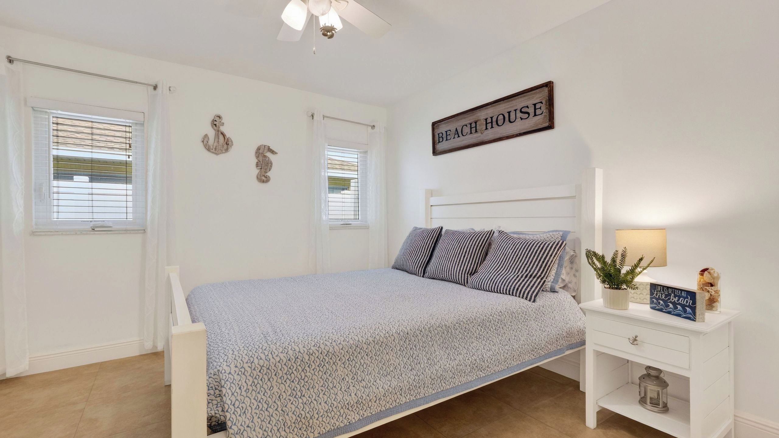 A bedroom with a bed, a nightstand, a wall-mounted sign, and a ceiling fan.