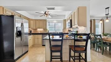 A modern kitchen with a central island, stainless steel appliances, and a ceiling fan.