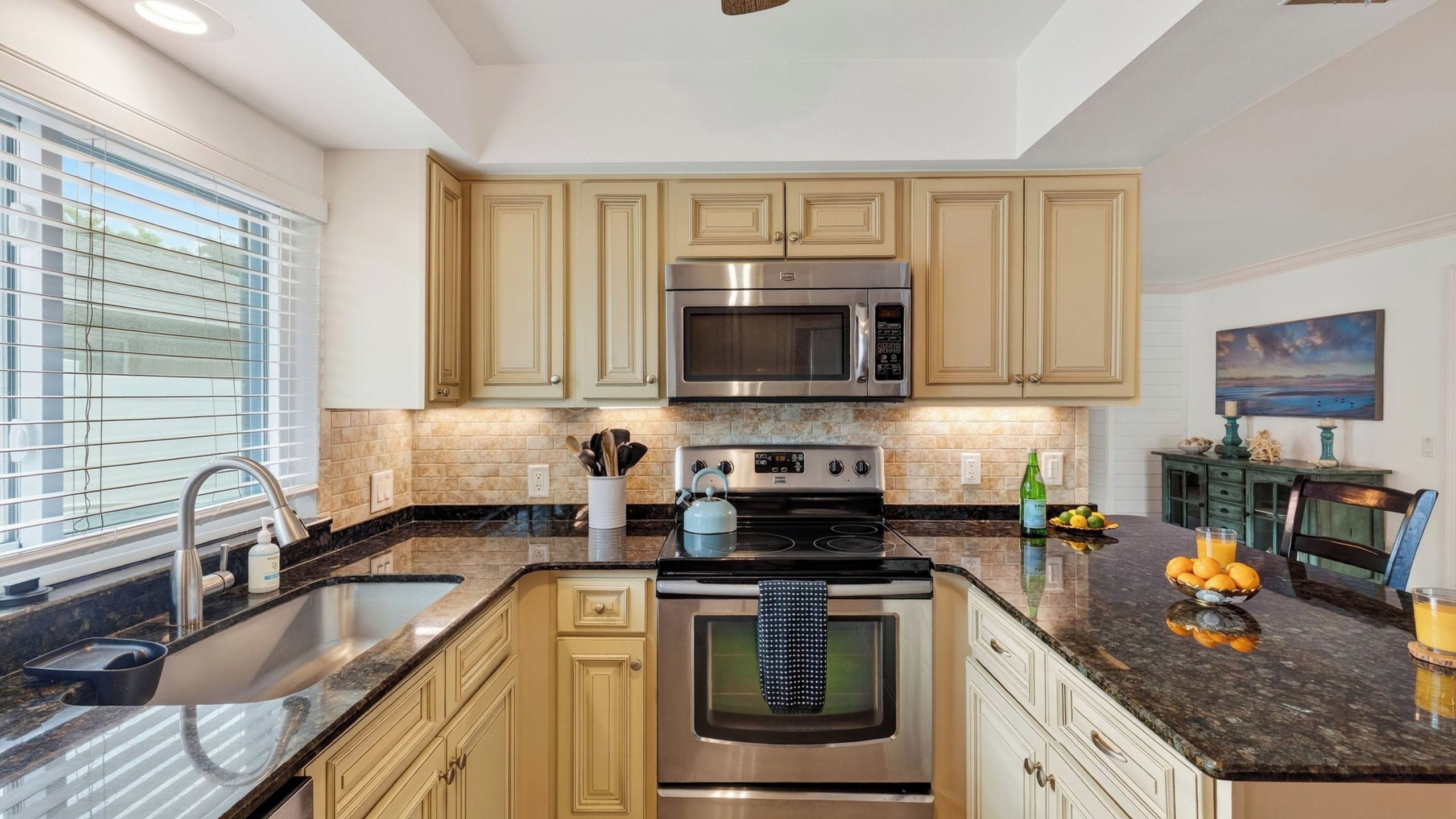 A modern kitchen with stainless steel appliances, a granite countertop, and beige cabinetry.