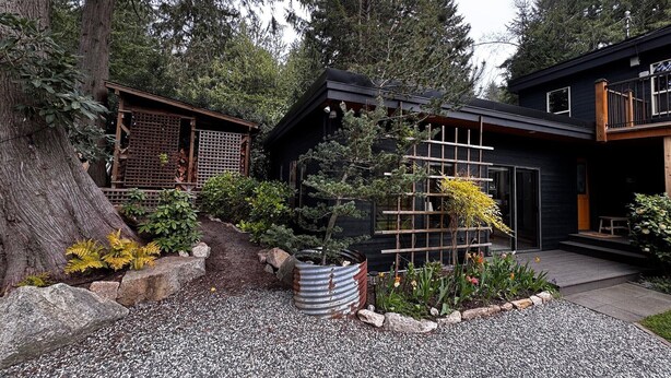 Ein modernes Haus mit einer Holterrasse, einem Garten mit verschiedenen Pflanzen und einem großen Baum.