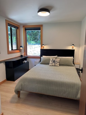 Un dormitorio con cama, lámparas de noche, mesita de noche, escritorio y ventana con vistas a zonas verdes.