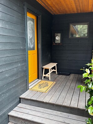 Een houten veranda met een gele deur, een klein houten tafeltje en een welkomstmat.