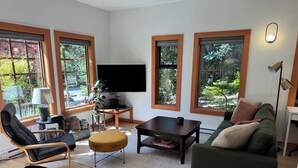 Ein modernes Wohnzimmer mit Flachbildfernseher, einer Couch, einem Couchtisch und einem Essbereich mit Holztisch.