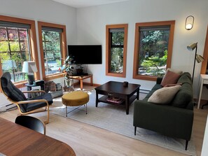 Una sala de estar moderna con un televisor de pantalla plana, un sofá, una mesa de centro y una zona de comedor con una mesa de madera.