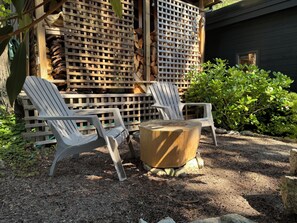 Eine Holzterrasse mit Adirondack-Stühlen und einem runden Holztisch.