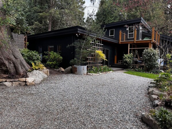 A two-story house with a gravel driveway leading to a wooden deck.